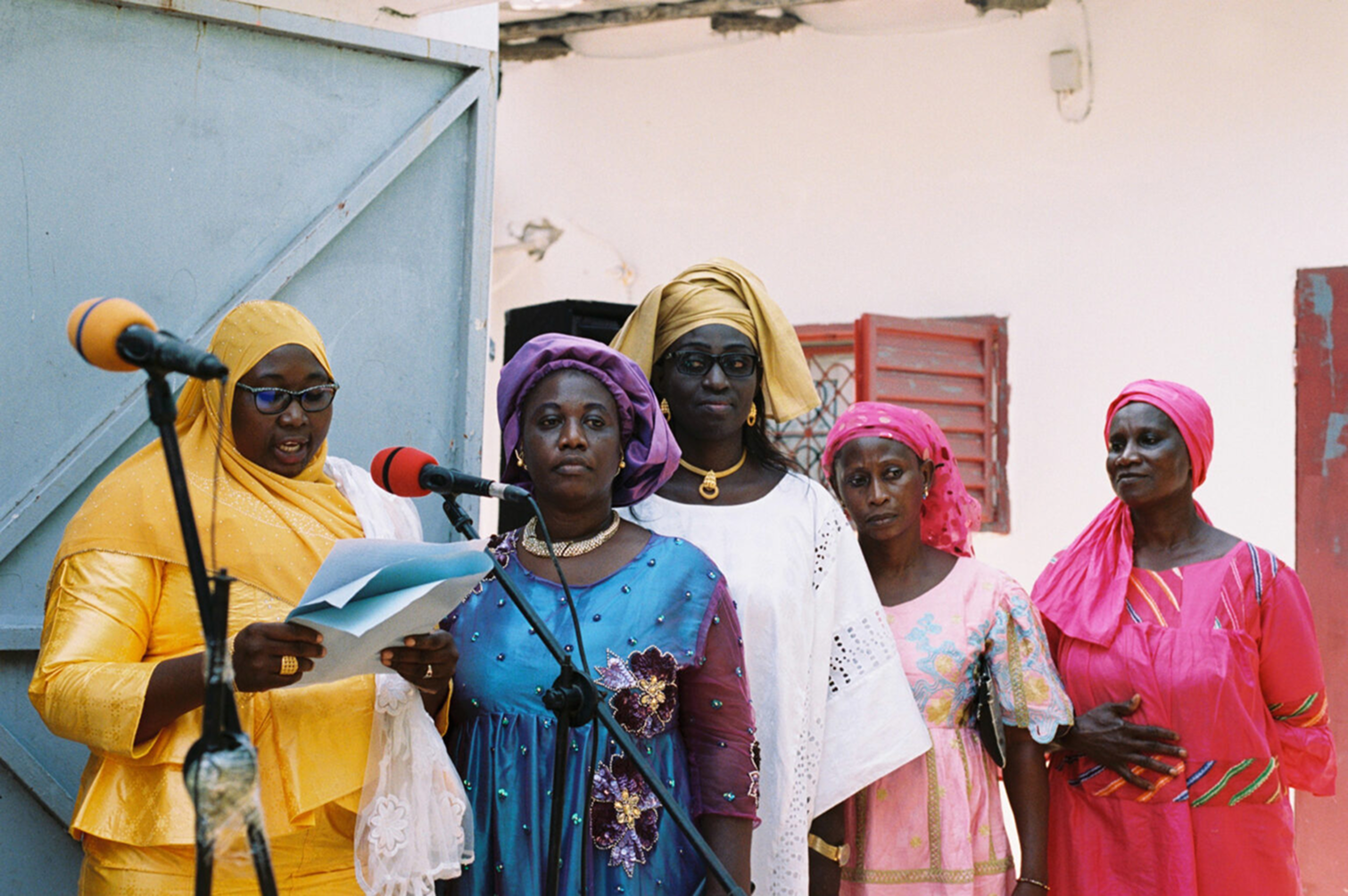 Group of women standing outdoors with microphones, possibly at a public event or meeting.
