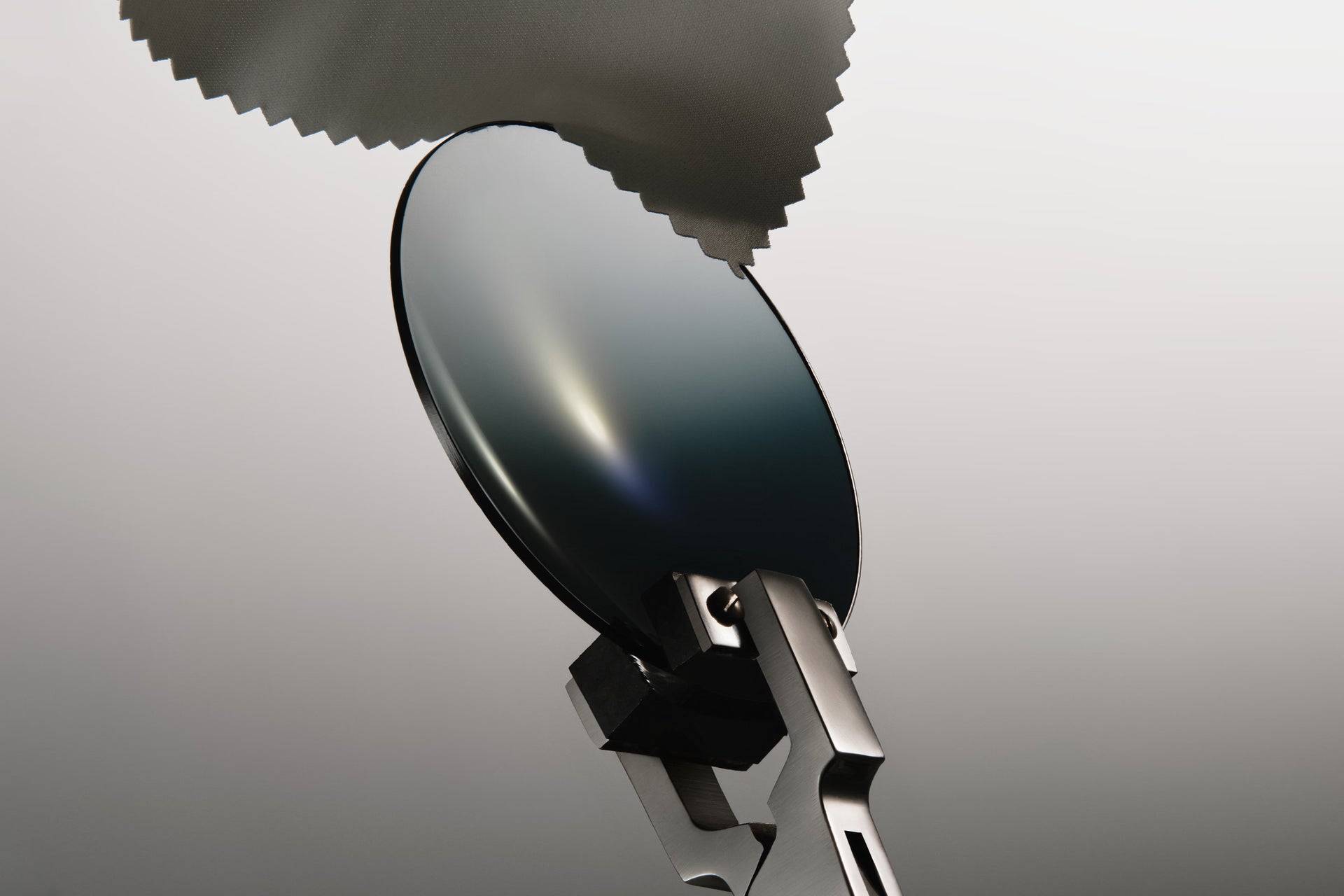 This image features a specialized optical lens cleaning cloth being used to wipe a camera lens or sunglasses.